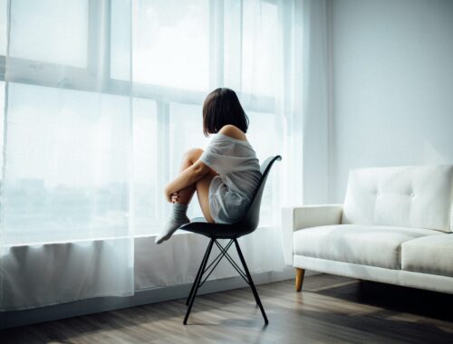 Woman sat on chair hugging her knees whilst staring out of window