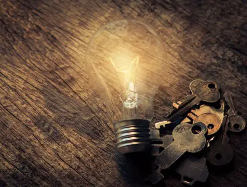 Glowing lightbulb on brown wooden table next to some keys