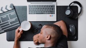 burn out- man sleeping at his desk with a laptop and cup of coffee
