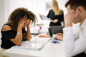woman looking stressed at a shared desk at work with a man sat opposite her