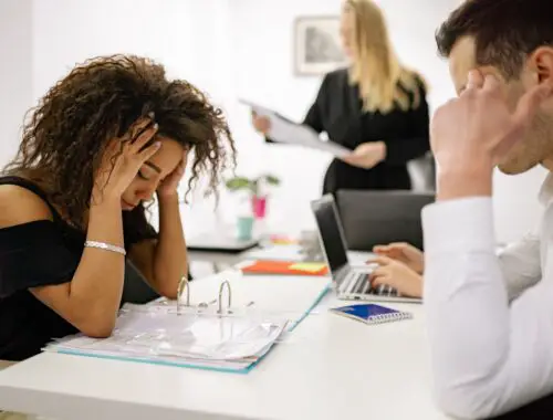 woman looking stressed at a shared desk at work with a man sat opposite her