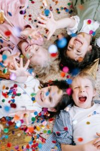 four happy children lying on the floor face up with confetti falling down on them showing their development
