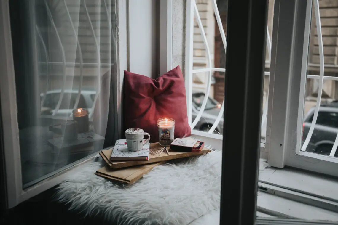 a window with a pillow, candle and drink