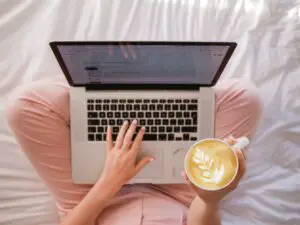 person sitting on a bed with laptop on knee and coffee, bird's eye view