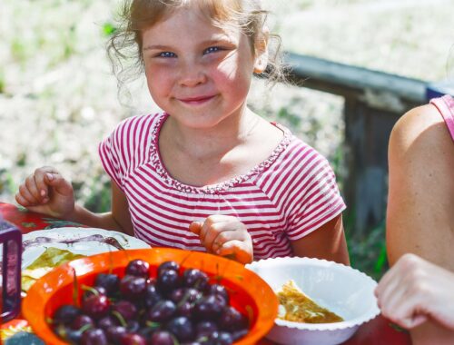 child with berries at a table outside smiling