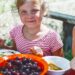 child with berries at a table outside smiling