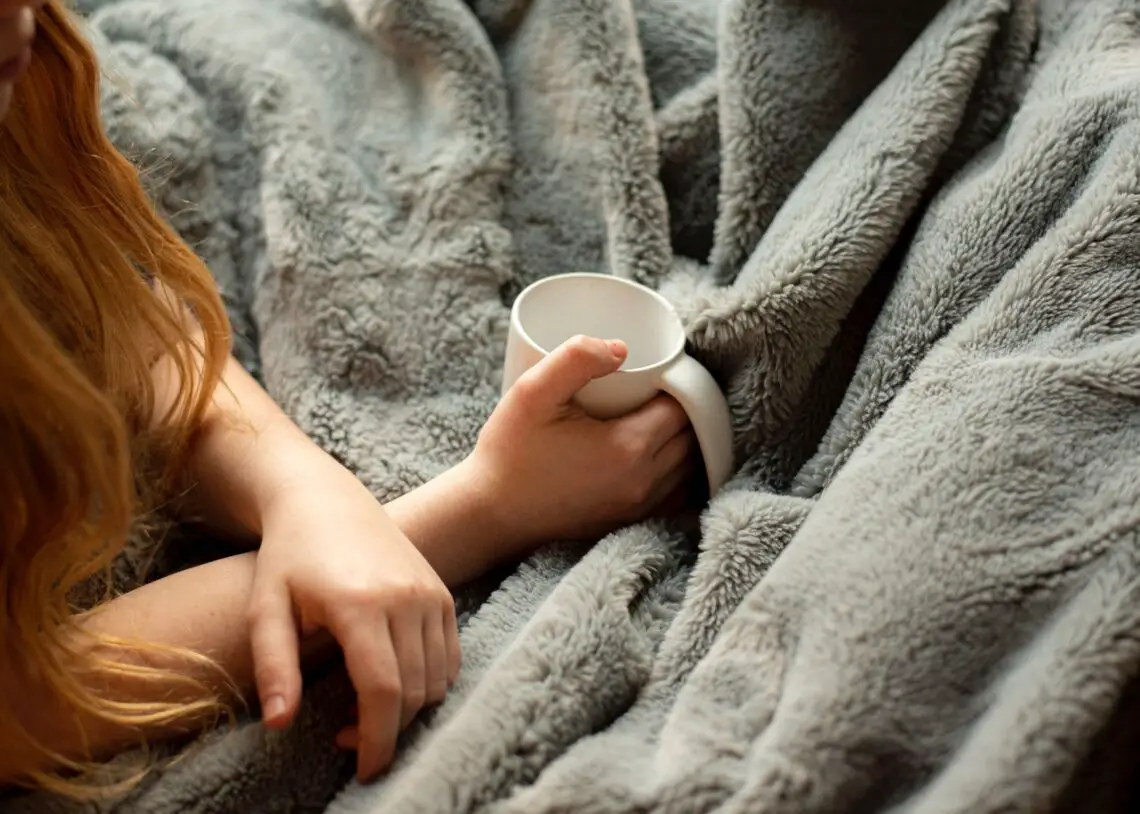 person under a blanket holding a mug