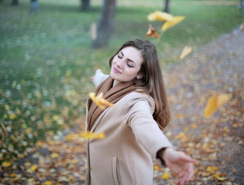 lady smiling with arms open with leaves falling around her