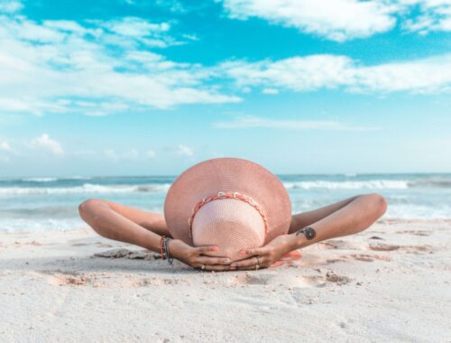 person laying back on a beach with blue sky - wearing a straw hat