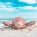 person laying back on a beach with blue sky - wearing a straw hat